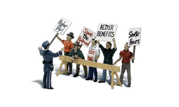 Picket Line - HO Scale - Five rowdy workers stand behind barricades holding picket signs, demanding shorter hours and better pay, while an officer of the law tries to keep the peace