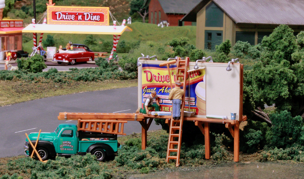 Sign Slingers - HO Scale - Two workers glue a sign in place on one side of a two-sided billboard